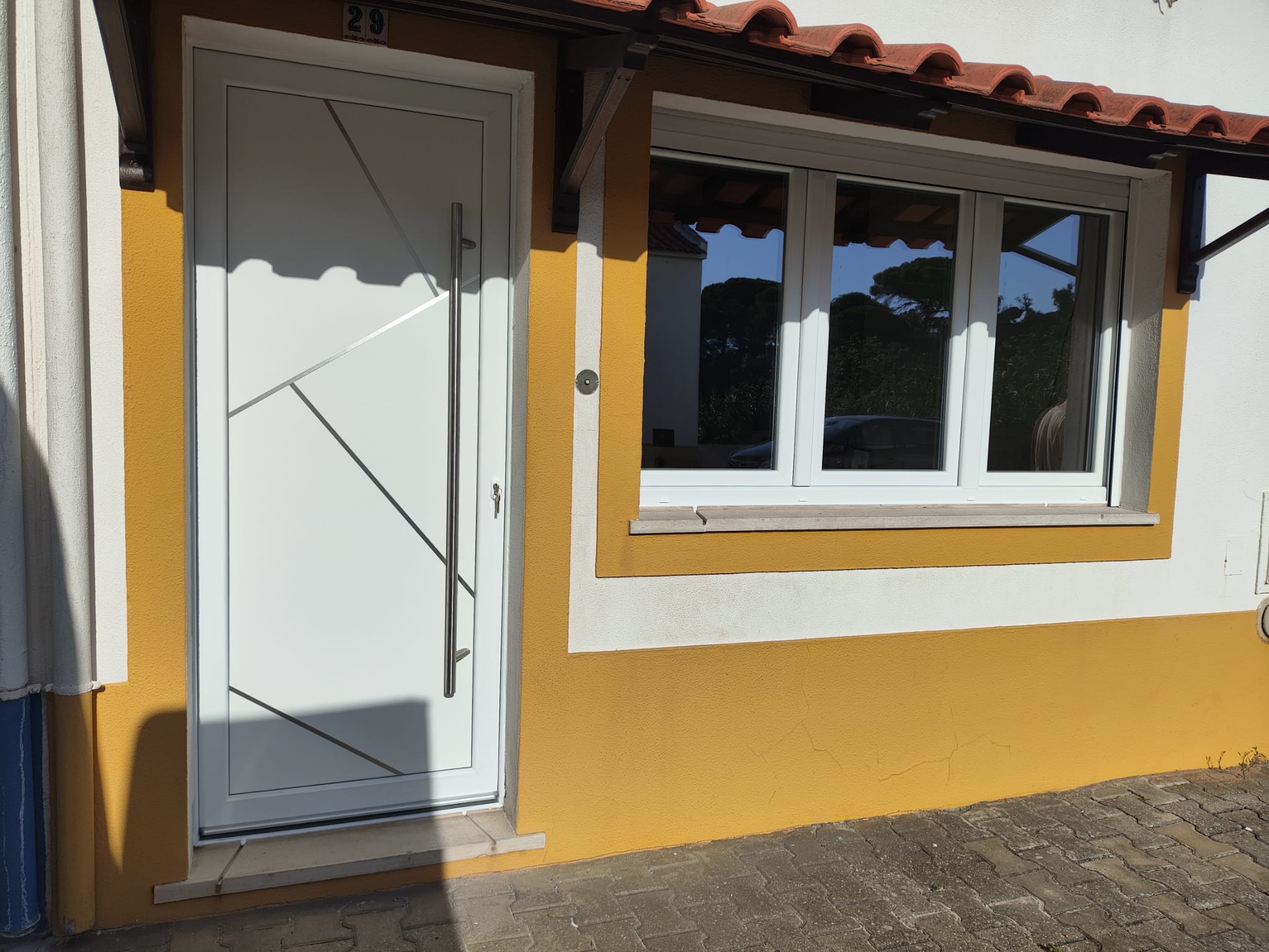 Porta de entrada em PVC branco com puxador em inox numa moradia